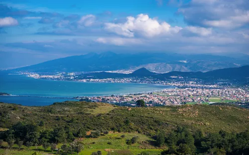 Küstenlandschaft mit Stadt, Hügeln und blauem Himmel im Hintergrund.