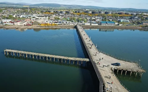 Luftansicht eines Piers, der ins Meer ragt, mit Stadt im Hintergrund.