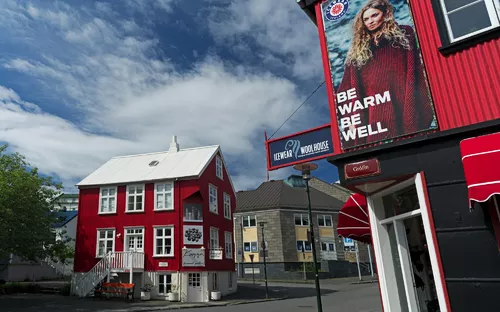 Rote Holzhäuser in einer Stadt mit blauem Himmel und Werbeposter an der Fassade.