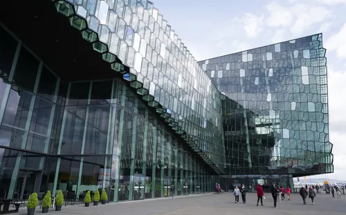 Moderne Glasfassade eines geometrisch gestalteten Gebäudes mit Personen davor.