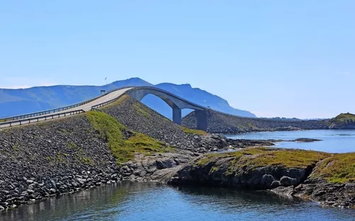 Eine kurvige Brücke führt über ein ruhiges Gewässer, umgeben von Bergen und bewachsenem Ufer.