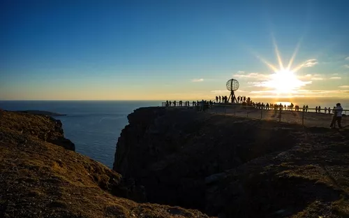 Klippenlandschaft mit Globus-Skulptur und Sonnenuntergang am Horizont.