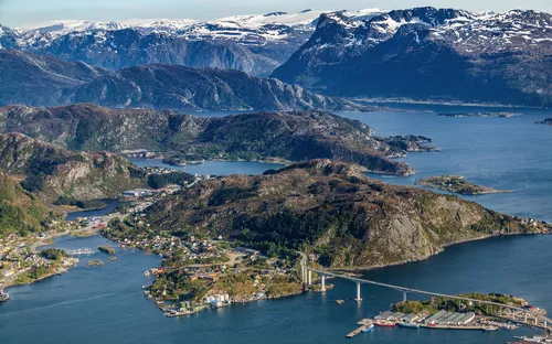 Küstenlandschaft mit Brücke, Häusern und Bergen im Hintergrund.