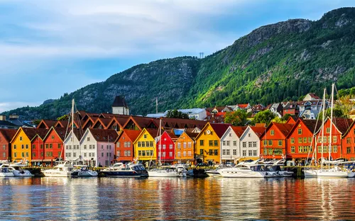 Bunte, traditionelle Holzhäuser am Wasser, Boote im Vordergrund, bewaldete Hügel im Hintergrund.