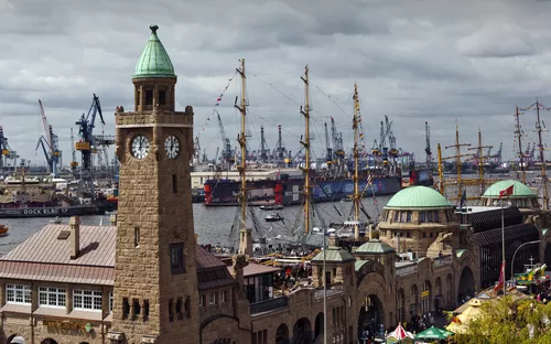 Hafengebäude in Hamburg mit Segelschiffen und Kränen im Hintergrund.