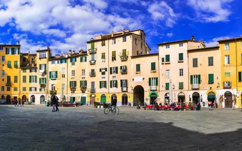 Historischer Platz mit bunten Gebäuden und Menschen unter blauem Himmel.