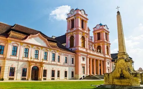 Barockes Kloster mit zwei Türmen und einem Obelisken im Vordergrund.