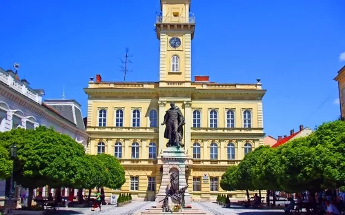 Altes Gebäude mit Turm und Statue auf einem Platz bei sonnigem Wetter.