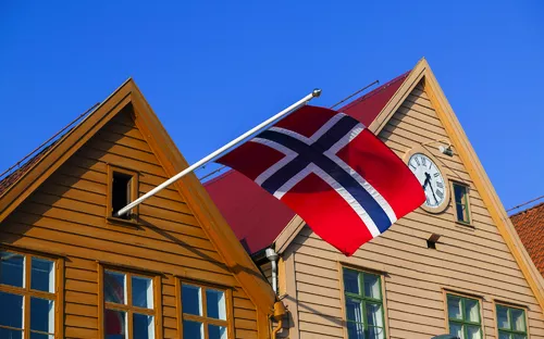 Norwegische Flagge an Holzhäusern mit Uhr und blauem Himmel.