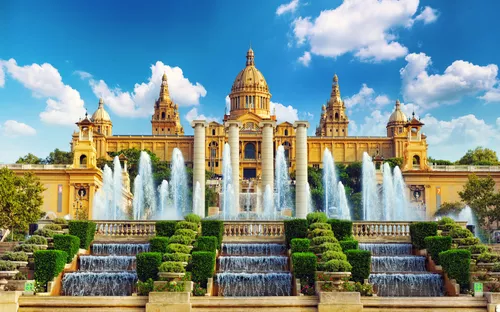 Palast mit Springbrunnen und grünen Gärten bei blauem Himmel.