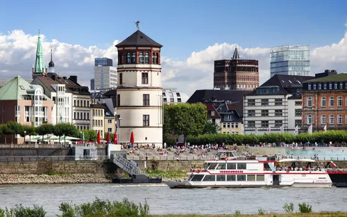 Stadtsilhouette mit einem Fluss, Booten und historischen Gebäuden im Vordergrund.