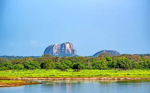 See mit Wald und zwei Hügeln im Hintergrund unter klarem Himmel.