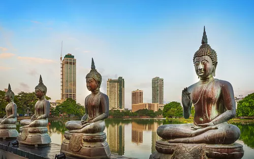 Reihe von Buddha-Statuen vor modernen Hochhäusern am Seema-Malaka-Tempel in Colombo, Sri Lanka.