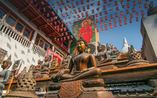 Mehrere Buddha-Statuen in einem buddhistischen Tempel unter bunten Flaggen.