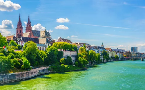 Blick auf Basels Rhein und die Altstadt mit Kirche im Hintergrund an einem sonnigen Tag.
