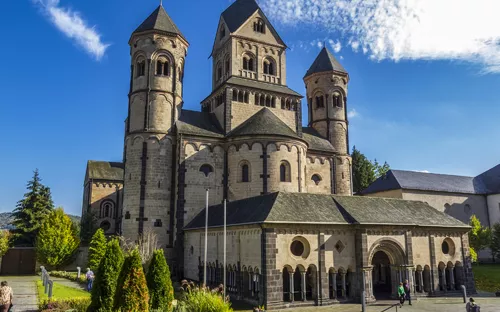 Romanische Kirche mit drei Türmen und blauem Himmel im Hintergrund.