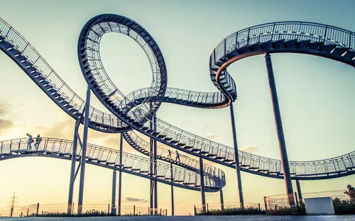 Stahlkonstruktion einer spiralförmigen Achterbahn mit Menschen bei Sonnenuntergang.