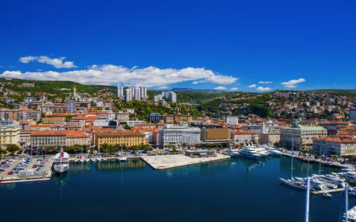Stadtpanorama mit Hafen und Segelbooten an einem sonnigen Tag.