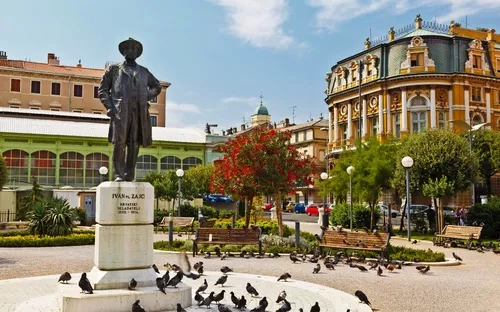 Statue von Ivan Zajc auf einem Platz mit historischen Gebäuden und Tauben.