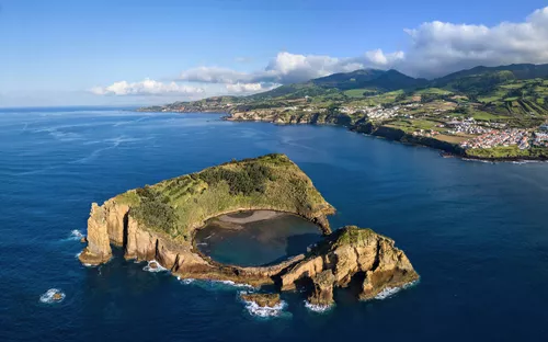 Luftaufnahme einer Insel mit Vulkankrater im Meer, grüne Hügel im Hintergrund.