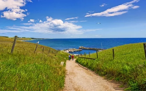 Weg führt zum Meer, Himmel mit Wolken, grüne Wiesen, kleine Anlegestelle.