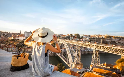 Person mit Hut sitzt vor Aussicht auf Stadt und Brücke.