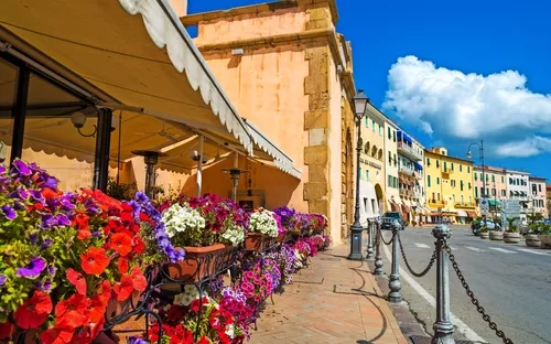 Straßencafé mit blühenden Blumen vor historischen Gebäuden an einem sonnigen Tag.