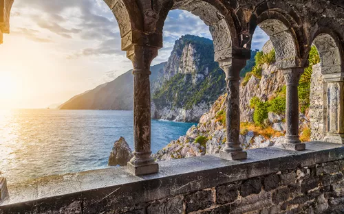 Blick durch Steinarkaden auf Küste und Meer bei Sonnenuntergang.