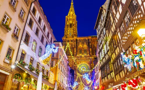 Straßenszene mit beleuchteter Kathedrale und Weihnachtsdekorationen am Abend.