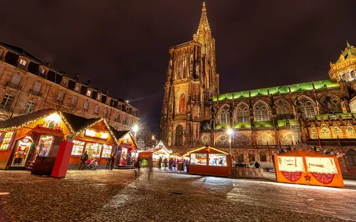Weihnachtsmarkt bei Nacht vor beleuchteter Kathedrale.
