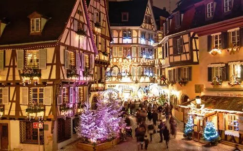 Beleuchtete Fachwerkhäuser bei Nacht in einer festlich geschmückten Stadt mit Weihnachtsmarkt.