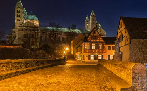 Pflasterstraße in der Nacht vor einer beleuchteten Kathedrale und Fachwerkhäusern.