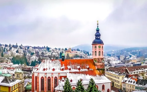 Panorama einer schneebedeckten Stadt mit Kirche und Hügeln im Hintergrund.