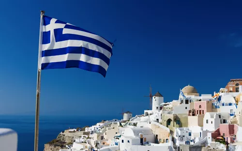 Griechische Flagge weht über weißen Häusern an einem sonnigen Hang.