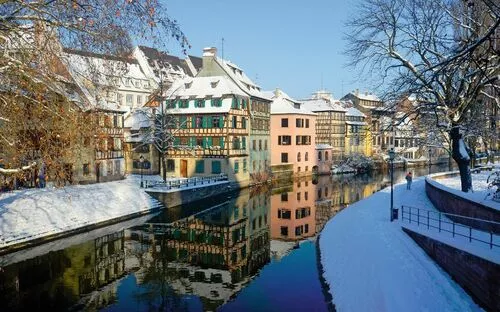 Verschneite Fachwerkhäuser spiegeln sich in einem Fluss.