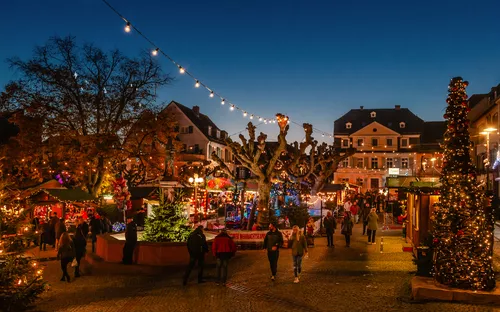 Weihnachtsmarkt mit Lichtern, Buden und Menschen bei Abenddämmerung.