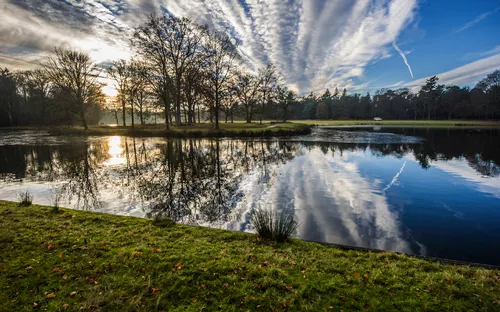 See mit Bäumen und Wolkenspiegelung im Wasser bei Sonnenuntergang.