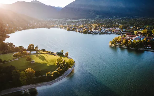 Luftaufnahme eines Sees mit umliegender Landschaft und Bergen im Hintergrund bei Sonnenuntergang