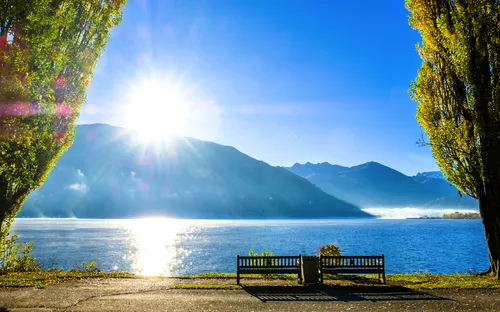 Sonnenaufgang über einem See mit Bergen im Hintergrund und Bäumen im Vordergrund.