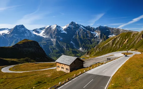 Straße mit Kurven vor schneebedeckten Bergen und blauem Himmel.