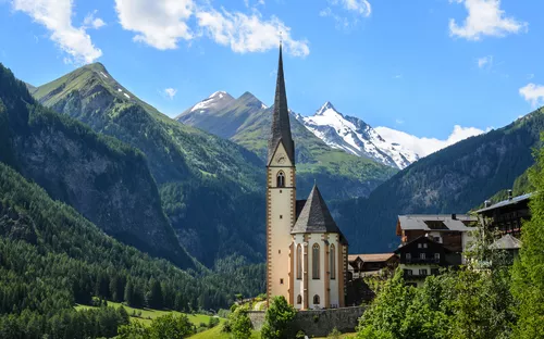 Kirche in alpiner Landschaft mit Bergen und blauem Himmel im Hintergrund.