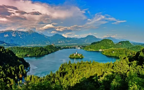 Blick auf einen smaragdgrünen See mit Insel und Kirche, umgeben von Bergen und Wäldern.