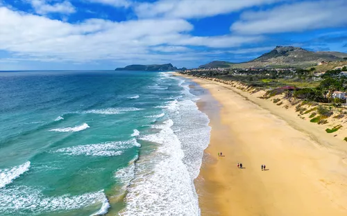 Langer Sandstrand mit blauem Meer und Hügel im Hintergrund unter blauem Himmel.