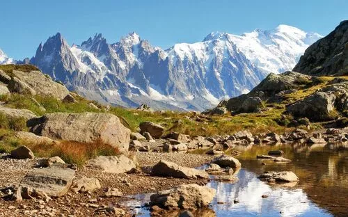 Blick auf den Mont Blanc in den Alpen, im Vordergrund ein kleiner Bach mit Steinen und Wiesen.
