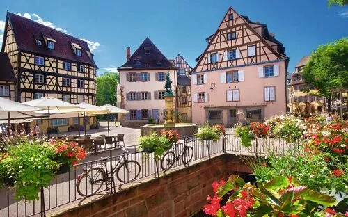 Fachwerkhäuser und Blumen auf einem Marktplatz bei sonnigem Wetter.