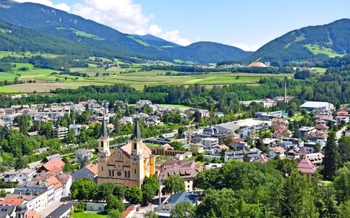 Stadt mit Kirche und umliegender Berglandschaft bei klarem Himmel.