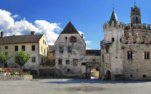 Mittelalterliche Burganlage mit Türmen und Zinnen unter blauem Himmel.