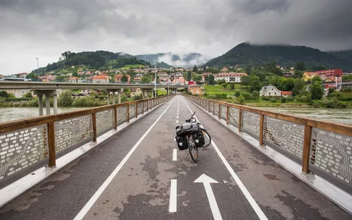 Fahrrad auf einer Brücke mit Blick auf eine Stadt und Berge im Hintergrund.
