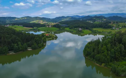 Landschaft mit See, Wäldern und Hügeln unter bewölktem Himmel.