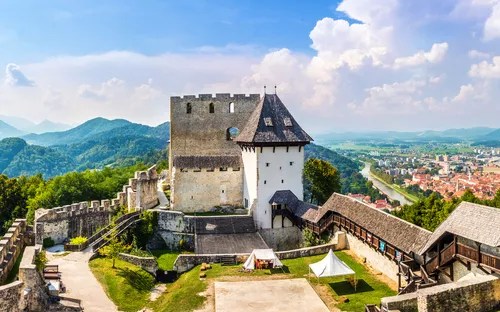 Burg auf einem Hügel mit Panoramablick auf Stadt und Berge im Hintergrund.